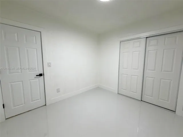 Neutral interior featuring smooth white walls, high-gloss floor tile, six-panel closet doors, and a six-panel entry door with matte black hardware