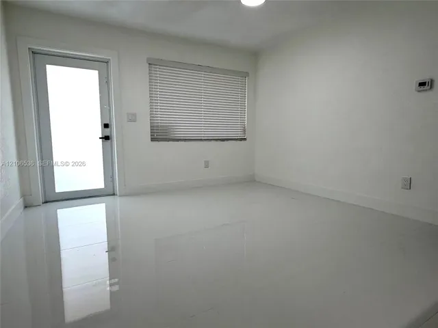 Interior space featuring polished white flooring, neutral wall finishes, a single-lite glass entry door, and a horizontal window with integrated blinds