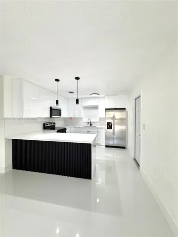 Kitchen featuring high-gloss white cabinetry, a center island with black vertical slat detailing, white stone-finish countertops, stainless steel appliances, and polished tile flooring