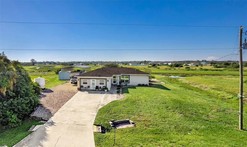 Single-story residence featuring a concrete driveway, attached metal carport, and expansive open acreage