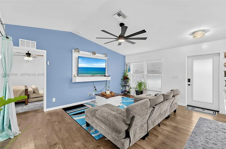 Vaulted ceiling featuring a multi-blade matte black ceiling fan, wood-finish flooring, and built-in floating media console