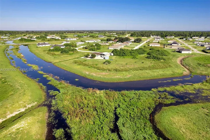 Aerial perspective of expansive acreage featuring winding canal frontage and cleared open terrain