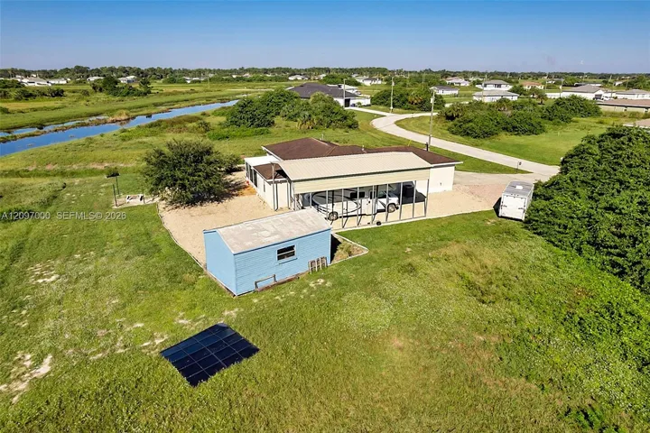 Aerial perspective of the property featuring a metal-roofed carport, detached storage structure, ground-mounted solar panels, and gravel surfacing