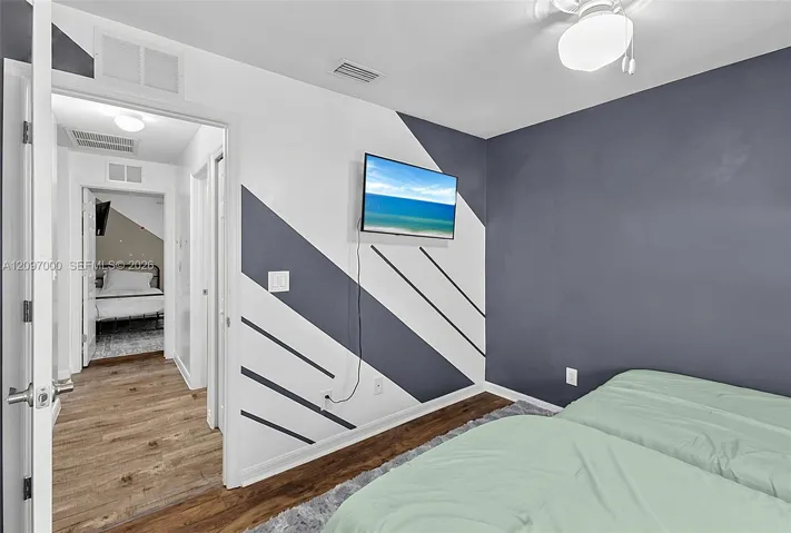 Wood-finish flooring, geometric-patterned accent wall, and ceiling-mounted light fixture with frosted glass globe