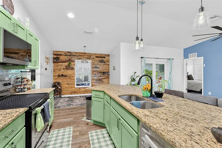 Kitchen featuring green cabinetry, stone-finish countertops, stainless steel dual-basin undermount sink, wood-finish flooring, and an accent wall with horizontal wood planks