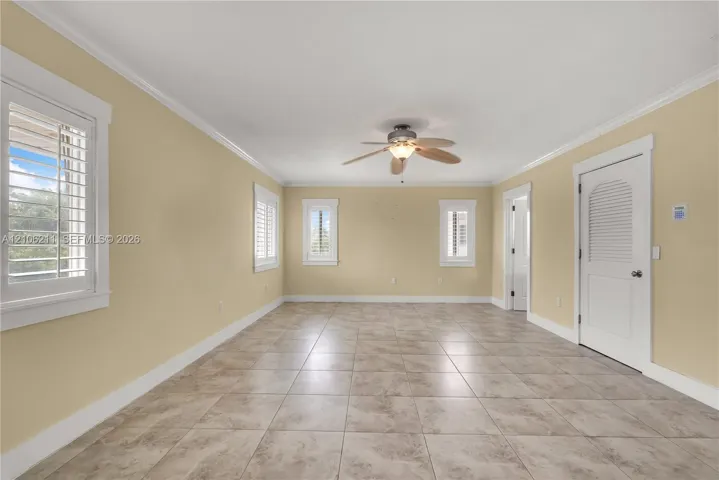 Spacious interior featuring neutral wall tones, ceramic tile flooring, plantation shutters, crown molding, and a central ceiling fan with an integrated light fixture