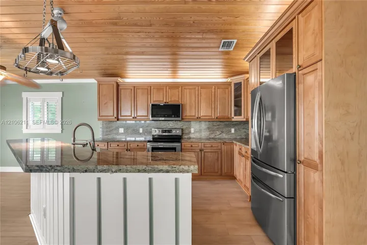 Kitchen featuring wood-paneled ceiling, custom cabinetry, stone-surfaced countertops, stainless steel appliances, and a center island with sink