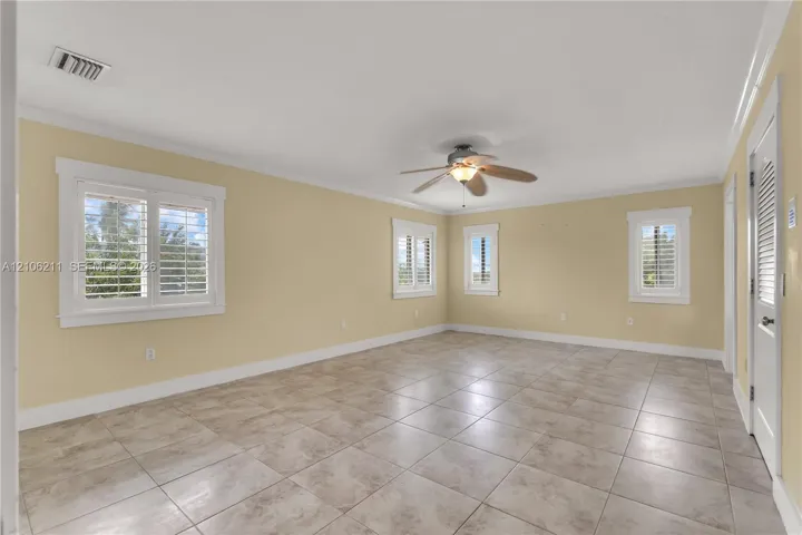 Neutral-toned interior room featuring large-format ceramic tile flooring, plantation shutters, and a ceiling fan with integrated lighting