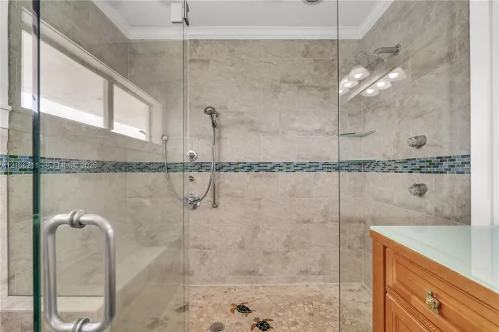 Walk-in shower featuring glass paneling, floor-to-ceiling tile with a decorative mosaic accent band, a built-in tiled bench, stone pebble flooring with inlaid tile motifs, and a multi-function shower system