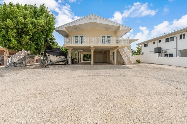 Stilt-construction home featuring a gravel driveway, an elevated deck with metal railing, and exterior stairs
