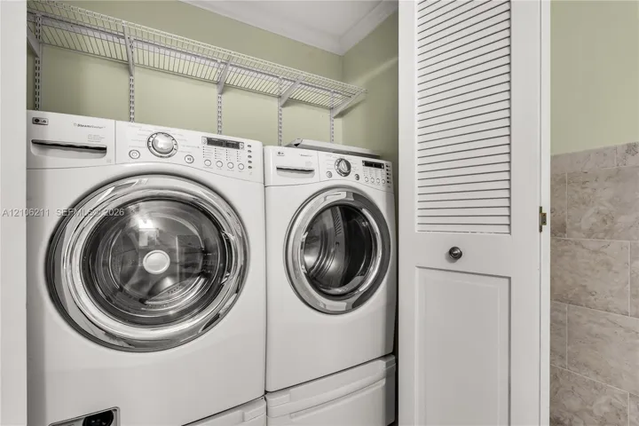 Laundry area featuring wall-mounted wire shelving, louvered closet doors, and tile wall surfacing