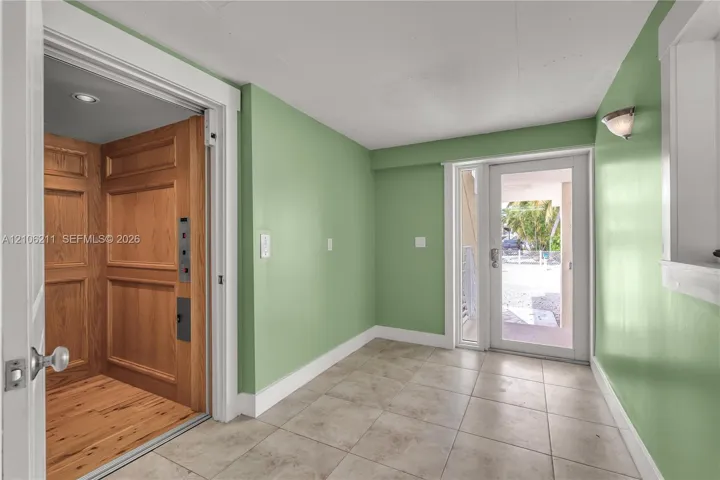 Interior elevator with wood-paneled walls and flooring, ceramic tile flooring, and glass-paned exterior door
