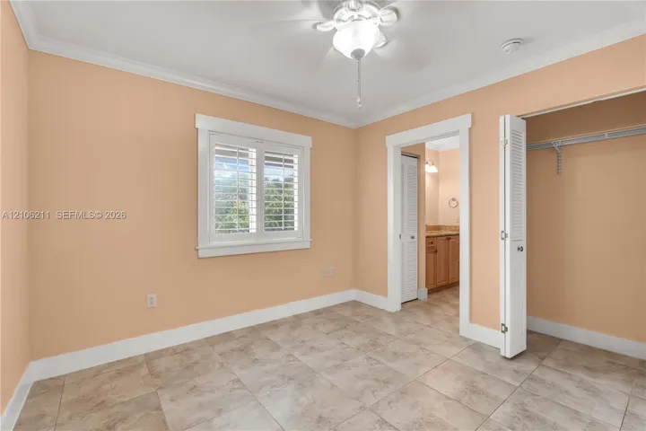 Neutral-toned room featuring ceramic tile flooring, crown molding, plantation shutters, a ceiling fan with integrated lighting, and a closet with bifold louvered doors