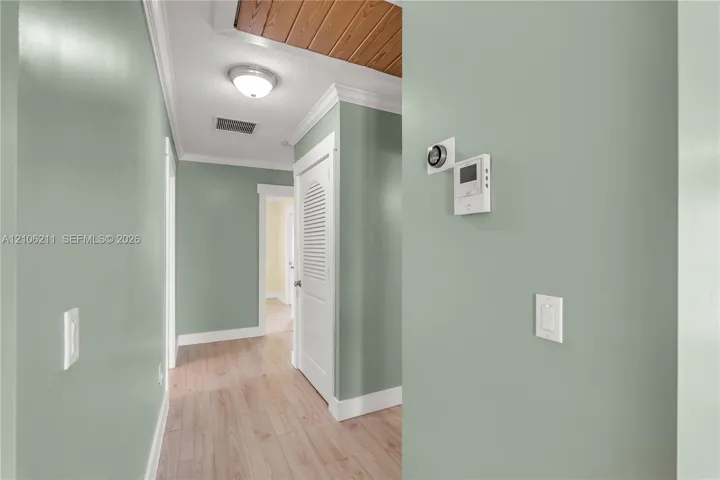 Hallway featuring wood-finish flooring, wood-paneled ceiling accent, crown molding, and a louvered-panel closet door