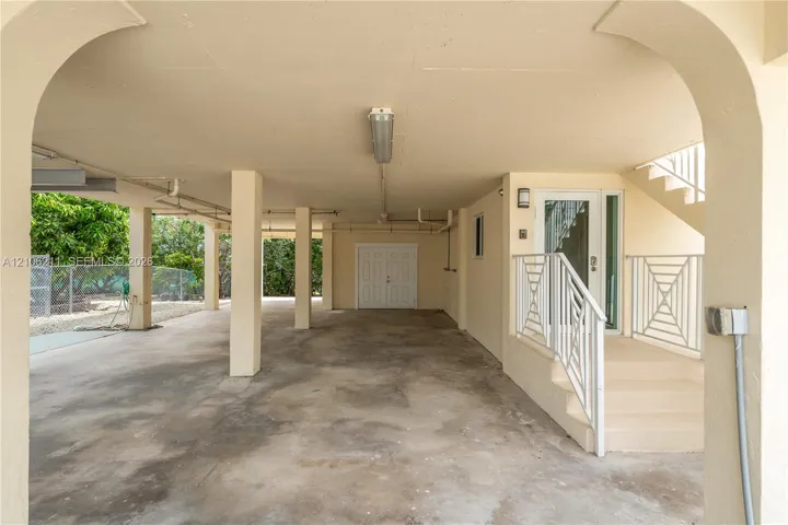 Covered carport with architectural archways, concrete flooring, dual-door utility entrance, and staircase with metal railings