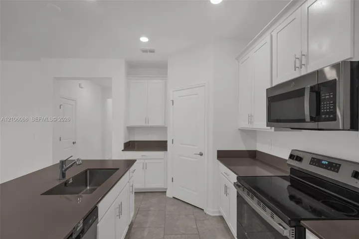 Kitchen featuring white cabinetry, solid-surface countertops, tile flooring, and stainless steel appliances