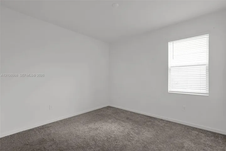 Neutral interior room featuring plush carpeting, white walls, and a window with horizontal blinds