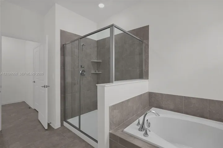 Walk-in shower with a glass enclosure, built-in shelving, and neutral tile surround, featuring a soaking tub with a deck-mounted chrome faucet and matching tile backsplash