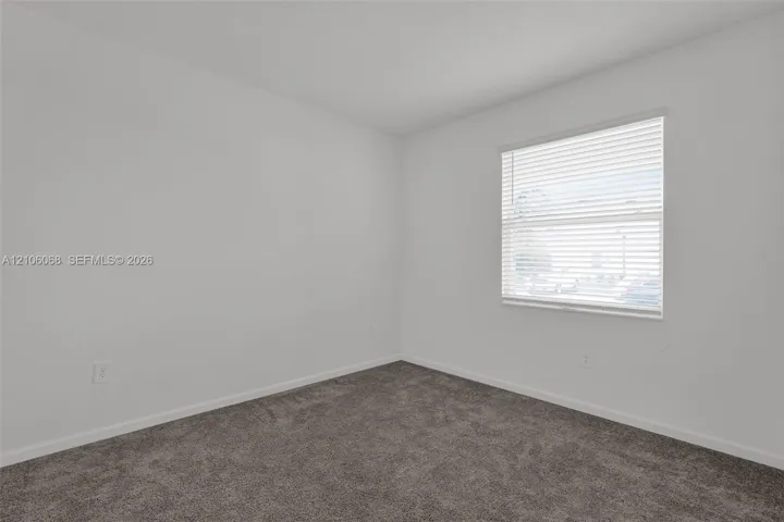 Room featuring neutral-toned carpeting, crisp white wall finishes, and a single-hung window with horizontal blinds