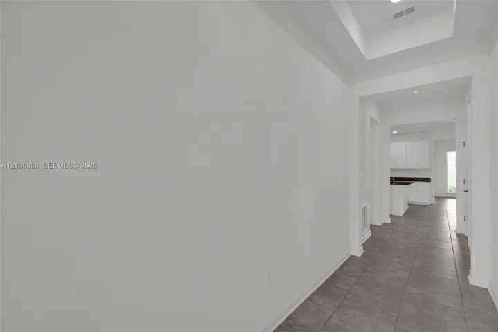 Interior hallway featuring neutral ceramic tile flooring and a recessed tray ceiling with inset lighting