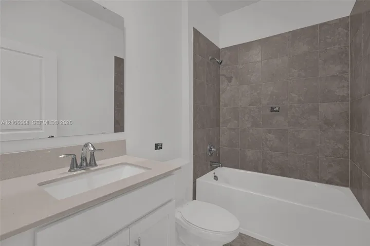 Bathroom featuring a white vanity with a light-toned solid surface countertop, an undermount sink, a wall-mounted mirror, and a bathtub with a tiled surround