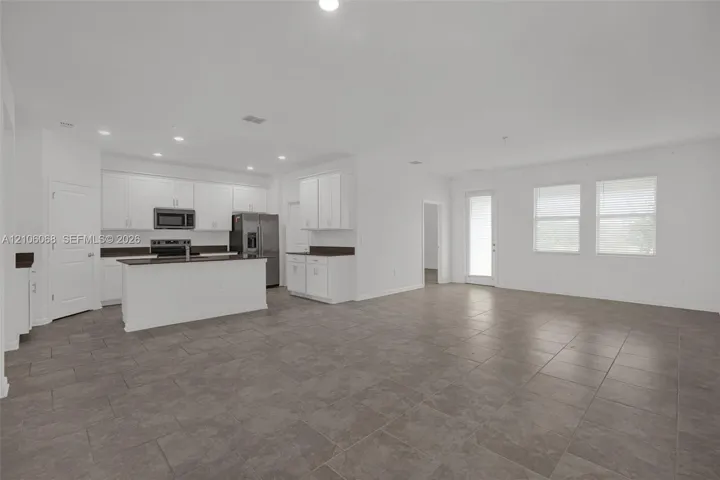 Open-concept interior featuring large-format tile flooring, recessed lighting, white cabinetry, a kitchen island with stone-surface countertops, and multiple windows