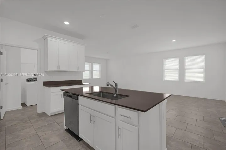 Kitchen featuring white cabinetry, solid-surface countertops, center island with an integrated stainless steel sink, recessed lighting, and tile flooring