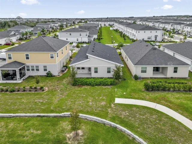 Aerial perspective of residential exteriors featuring gable rooflines, exterior stucco siding, covered concrete patios, and established landscaping
