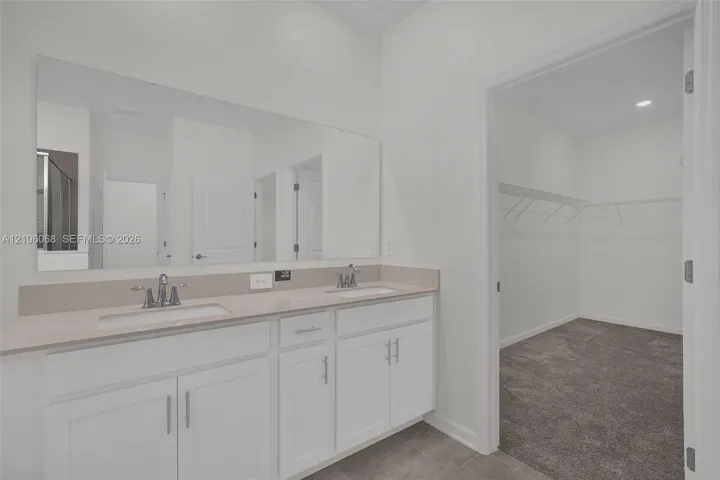 Double vanity featuring white cabinetry, quartz-surface countertops, integrated dual sinks, and a full-width wall mirror