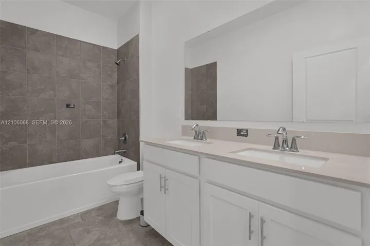 Double vanity featuring white cabinetry, stone-composite countertops, and dual undermount sinks, complemented by a full-width vanity mirror and a shower-tub combination with large-format tile surround