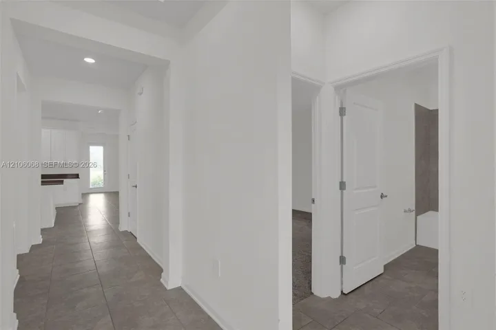 Interior hallway featuring large-format neutral floor tile, recessed lighting, and white interior doors