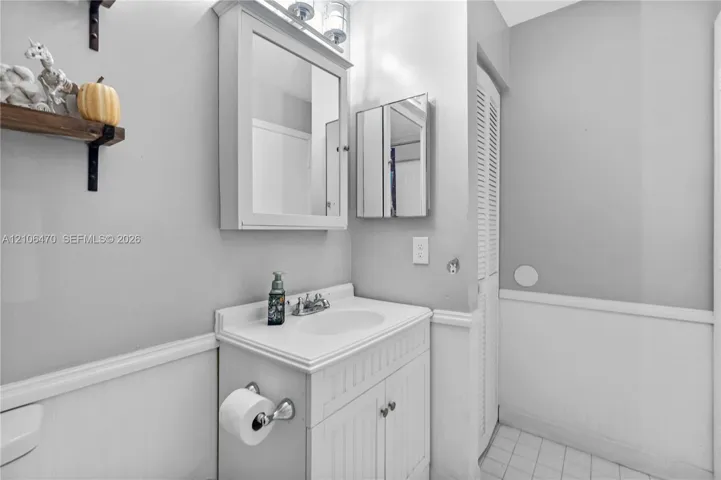 Vanity with beadboard cabinet doors, integrated sink, chrome faucet, mirrored medicine cabinet, and white tile flooring