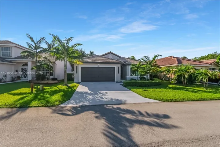 Stucco exterior residence featuring a concrete tile roof, attached two-car garage, concrete driveway, and manicured landscaping