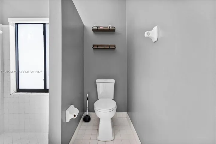 Bathroom featuring dual wood-finish wall shelves, a white vitreous china toilet, and square tile flooring