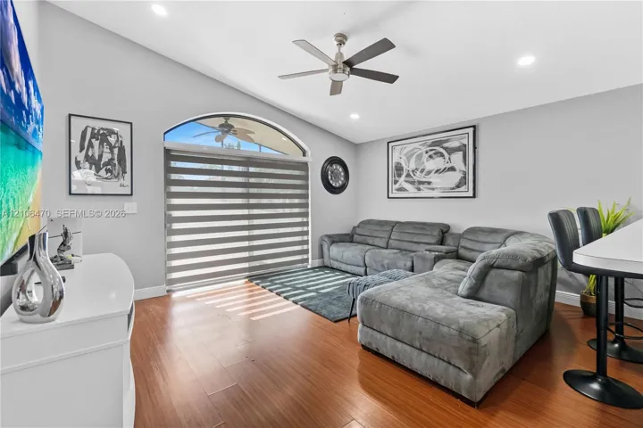 Vaulted ceiling featuring a central brushed-nickel ceiling fan, wood-finish flooring, and a large arched sliding glass door with integrated roller shades