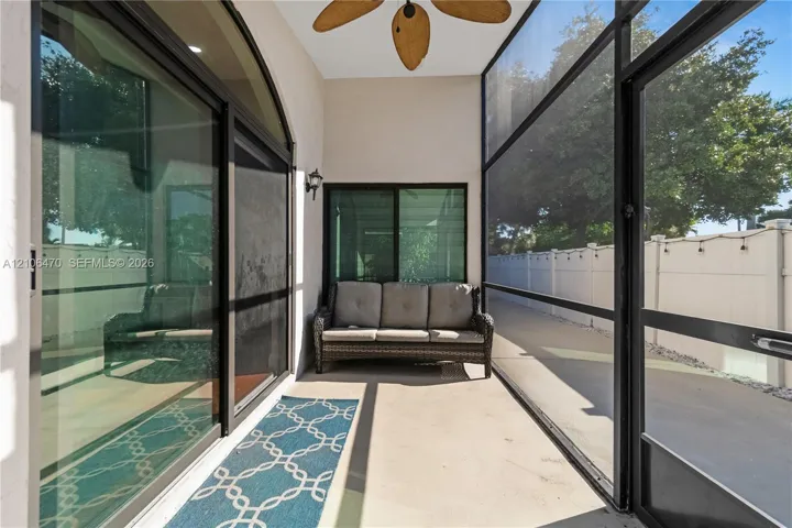 Screened lanai featuring concrete flooring, black-framed sliding glass doors, a ceiling-mounted fan, and an exterior wall light fixture
