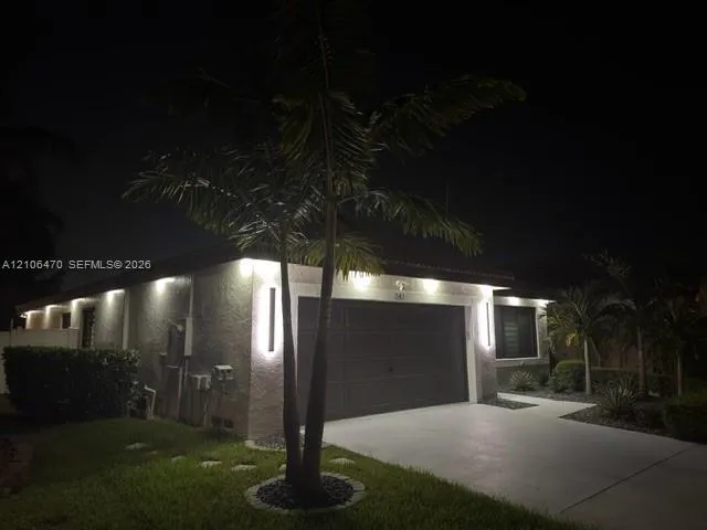 Exterior facade featuring stucco siding, a multi-car garage, recessed soffit lighting, vertical wall-mounted exterior light fixtures, and palm tree landscaping