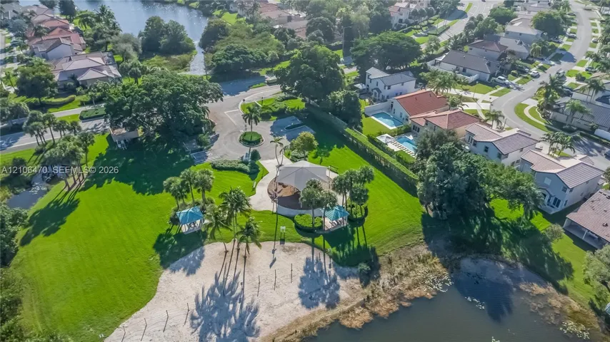 Community park area featuring an expansive lawn, shaded pavilion, sand beach, and mature palm trees situated along the water's edge