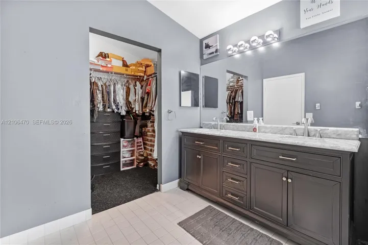 Dual-vanity cabinet with dark finish and light-toned stone countertop, large-format wall mirror, multi-bulb vanity light fixture, and built-in closet storage