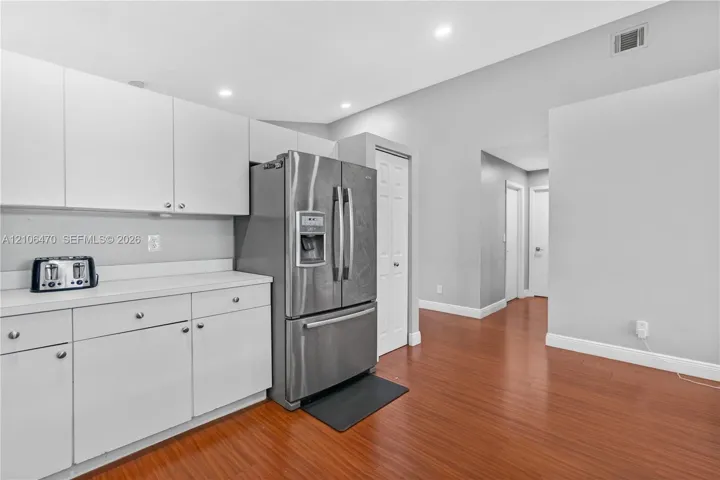 Kitchen featuring white cabinetry, wood-finish flooring, vaulted ceilings, recessed lighting, and a stainless steel refrigerator