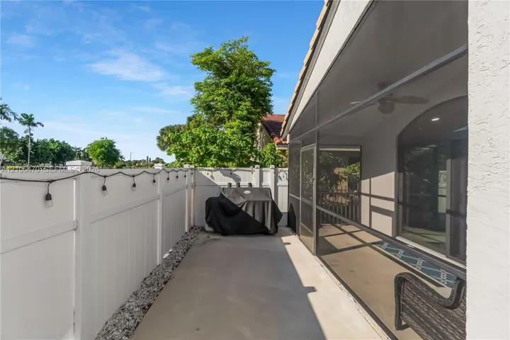 Screened-in patio featuring a concrete floor, ceiling fan, and white vinyl privacy fencing