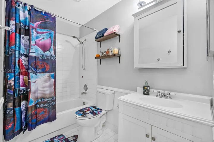 White vanity cabinet with an integrated sink, wall-mounted medicine cabinet, white tile shower surround, and two wood-finish wall-mounted shelves