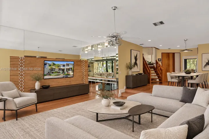 Living area featuring wood-finish flooring, a floor-to-ceiling mirrored wall, a slatted wood accent partition, a wood staircase, and recessed lighting