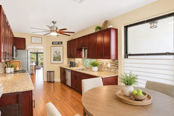 Kitchen featuring dark wood cabinetry, stone-finish countertops, a mosaic tile backsplash, stainless steel appliances, and wood-finish flooring