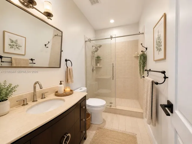 Bathroom featuring a dark-finish vanity with a neutral stone countertop, undermount sink, walk-in shower with sliding glass doors, and matte black hardware