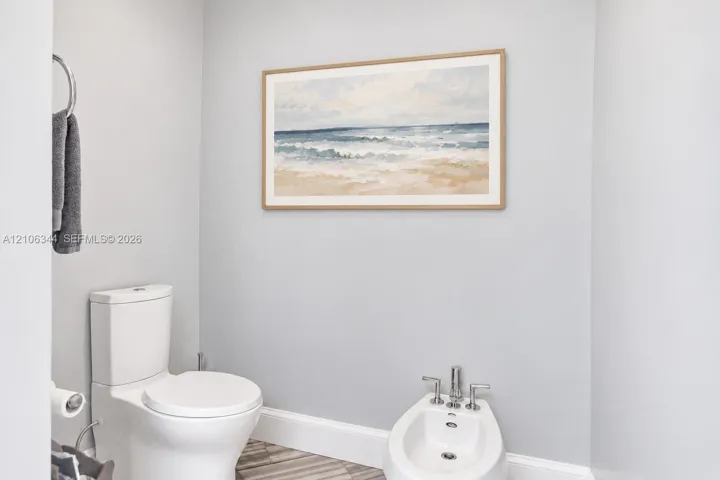 White porcelain toilet, bidet with chrome hardware, and metallic circular towel ring