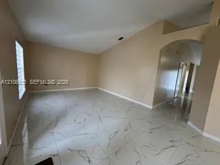 Interior room featuring vaulted ceilings, large-format tile flooring with a neutral veined pattern, and an arched architectural opening