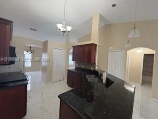 Kitchen featuring dark-toned cabinetry, stone-finish countertops, tile flooring, arched entryways, and multi-light hanging fixtures