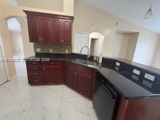 Kitchen featuring dark wood cabinetry, stone countertops, mosaic tile backsplash, dual-basin stainless steel sink, and large-format tile flooring
