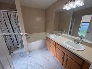Dual-sink vanity with wood-finish cabinetry, solid surface countertop, large wall-mounted mirror, and tile flooring